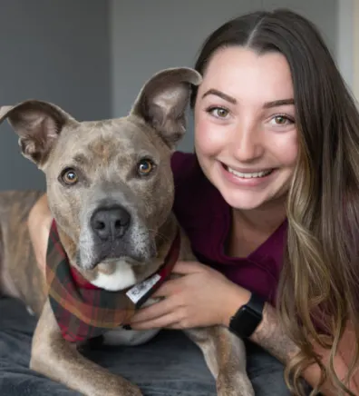 Claire smiling with a brown Pitbull with a checkered bandana on